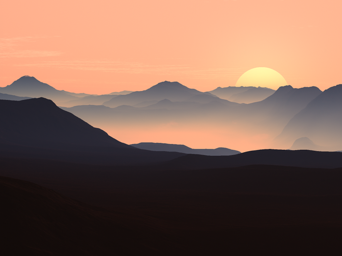 The silhouettes of mountains at dusk as the sun sets in an orange haze.