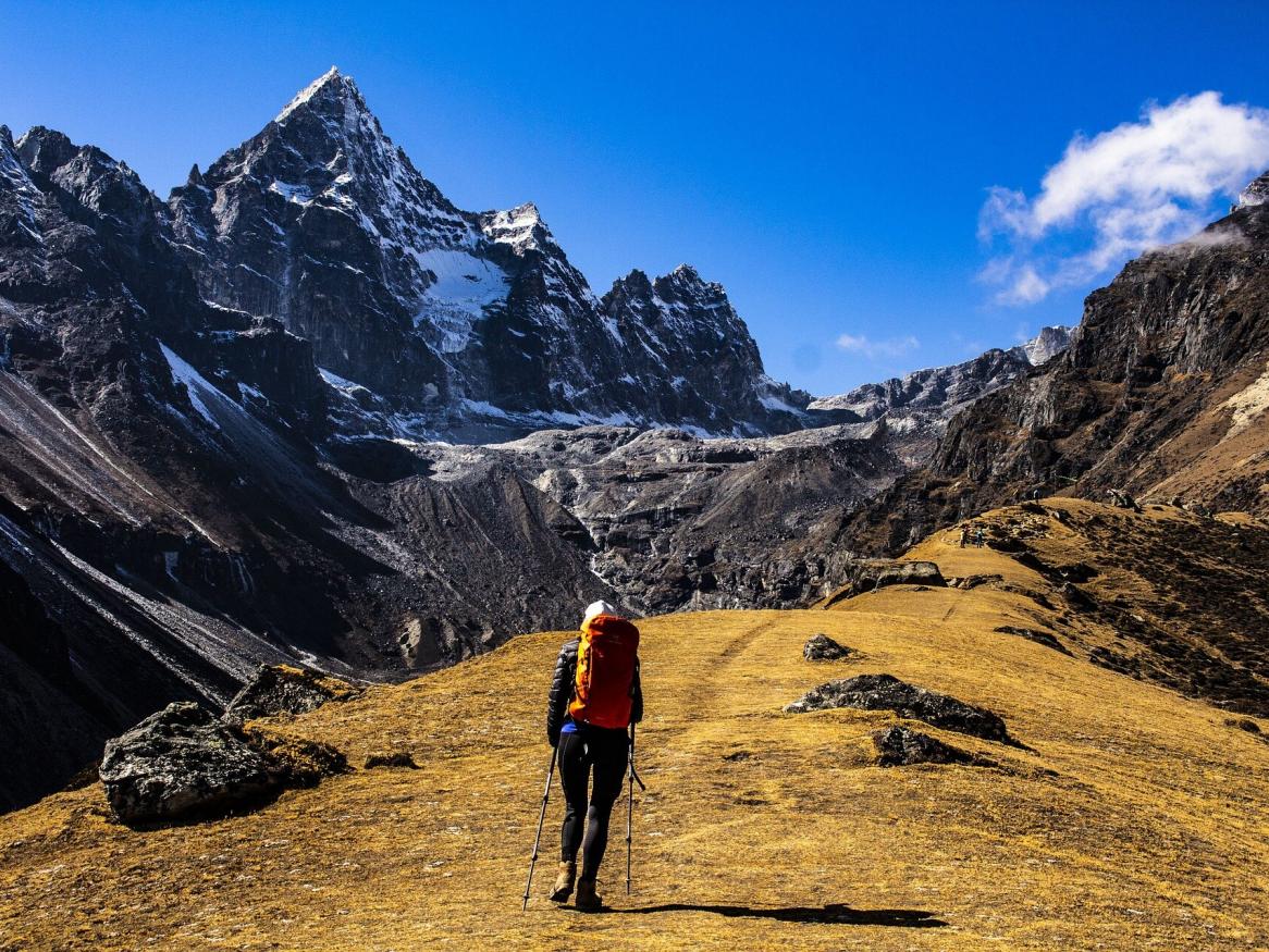 Photo of the back of a climber ascending Mount Everest, blue sky and clouds above one of the peaks