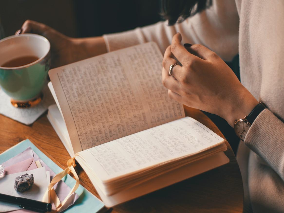 Someone writing in a journal while holding a cup of coffee