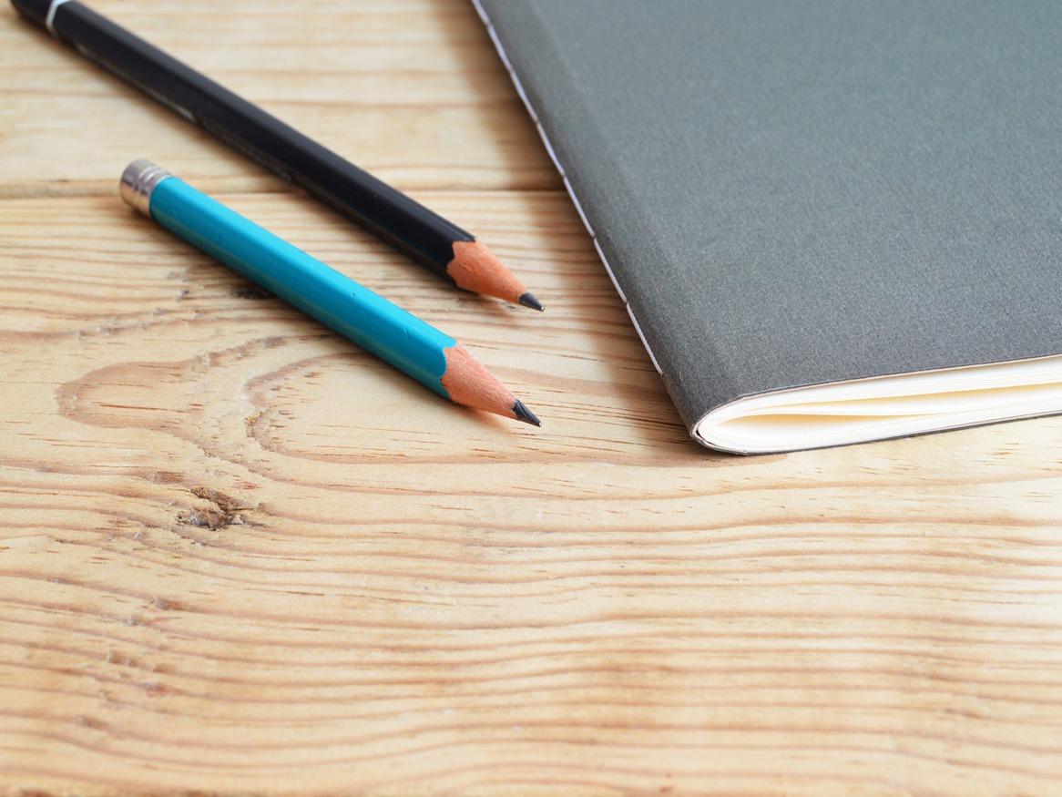 A notebook and two pencils on a wooden table