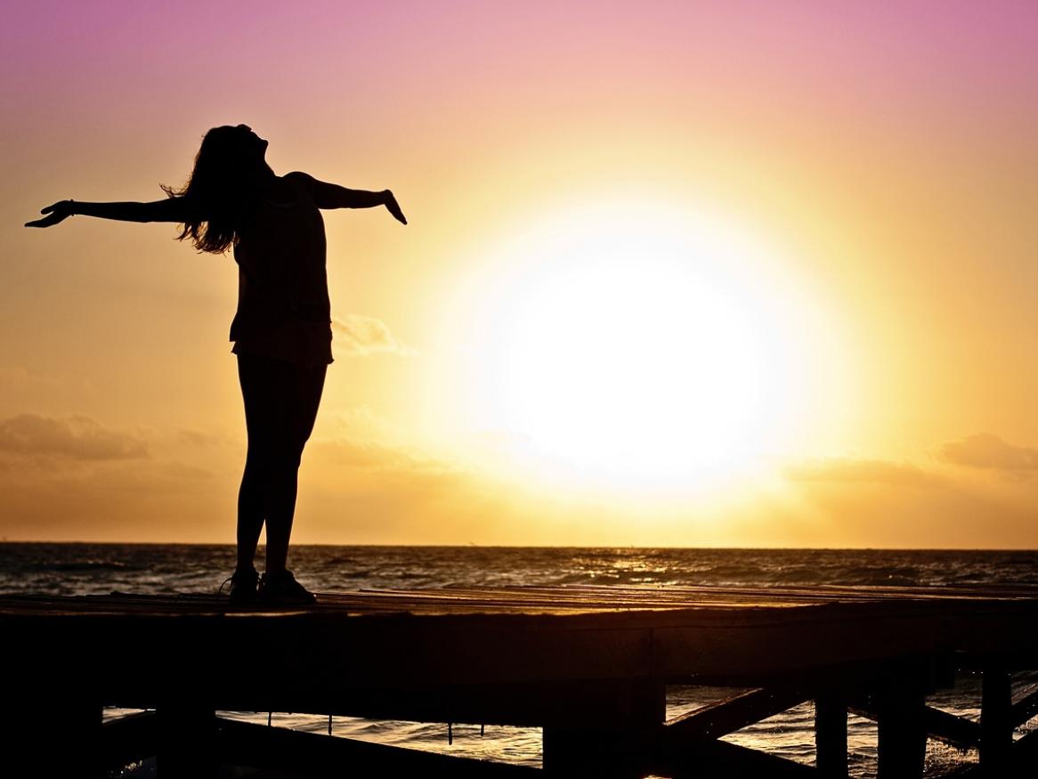 A person stands with their arms out in front of a sunset.