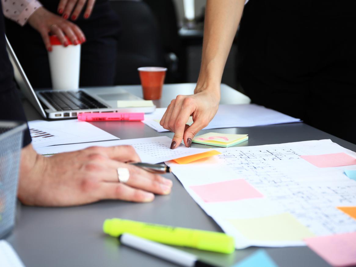 People's hands on a desk at meeting with post-it notes