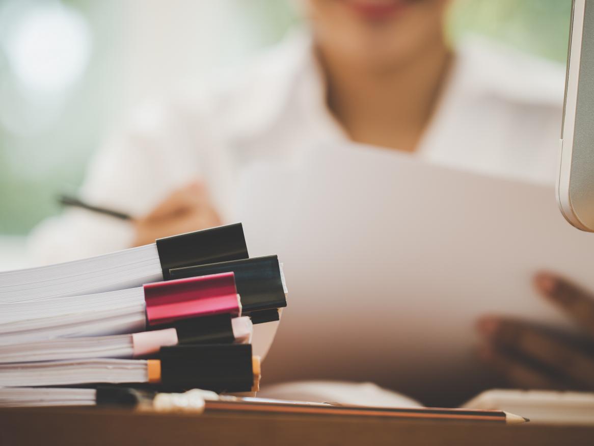 Woman at desk with computer and stack of papers