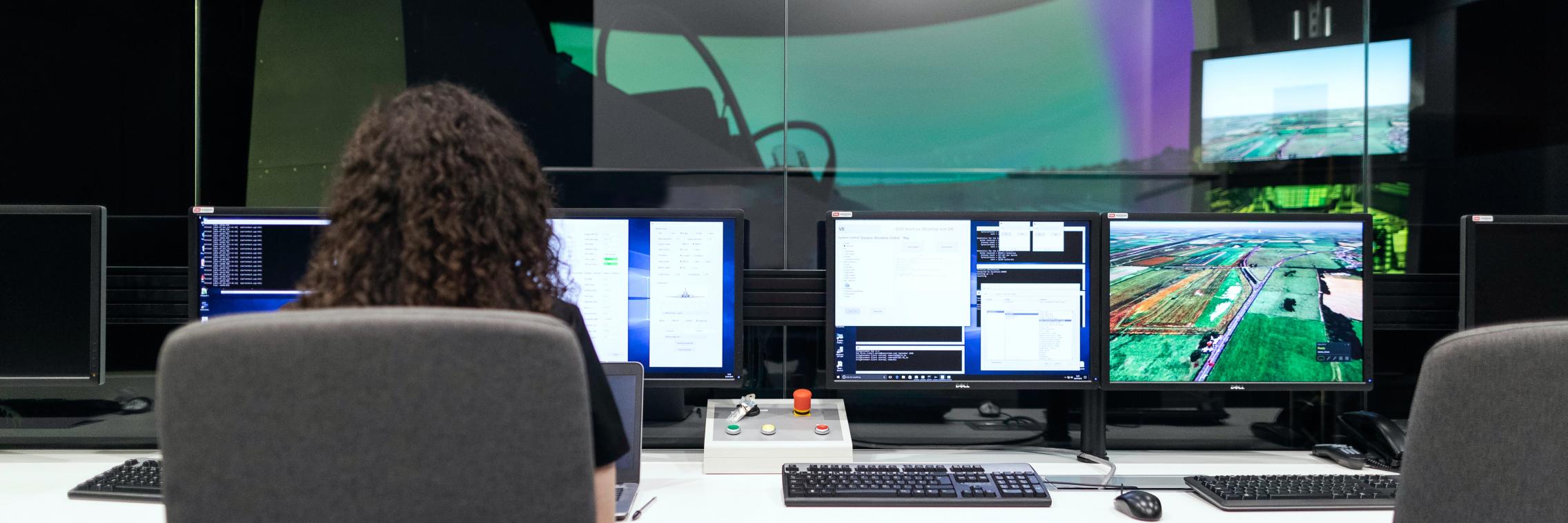 A woman sits at several computer monitors