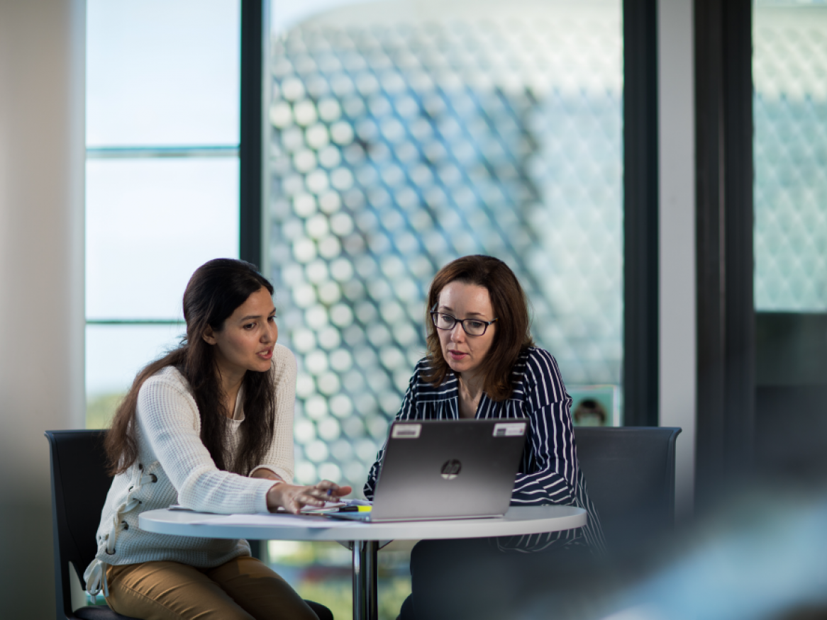 2 people sitting at a table with computer