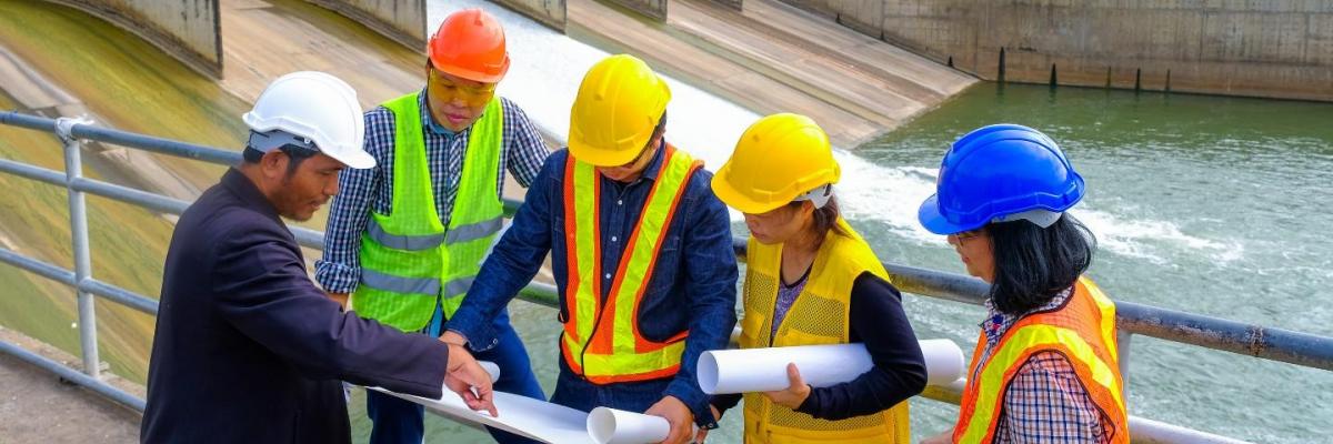 Staff in high-vis clothing, looking at plans, near water