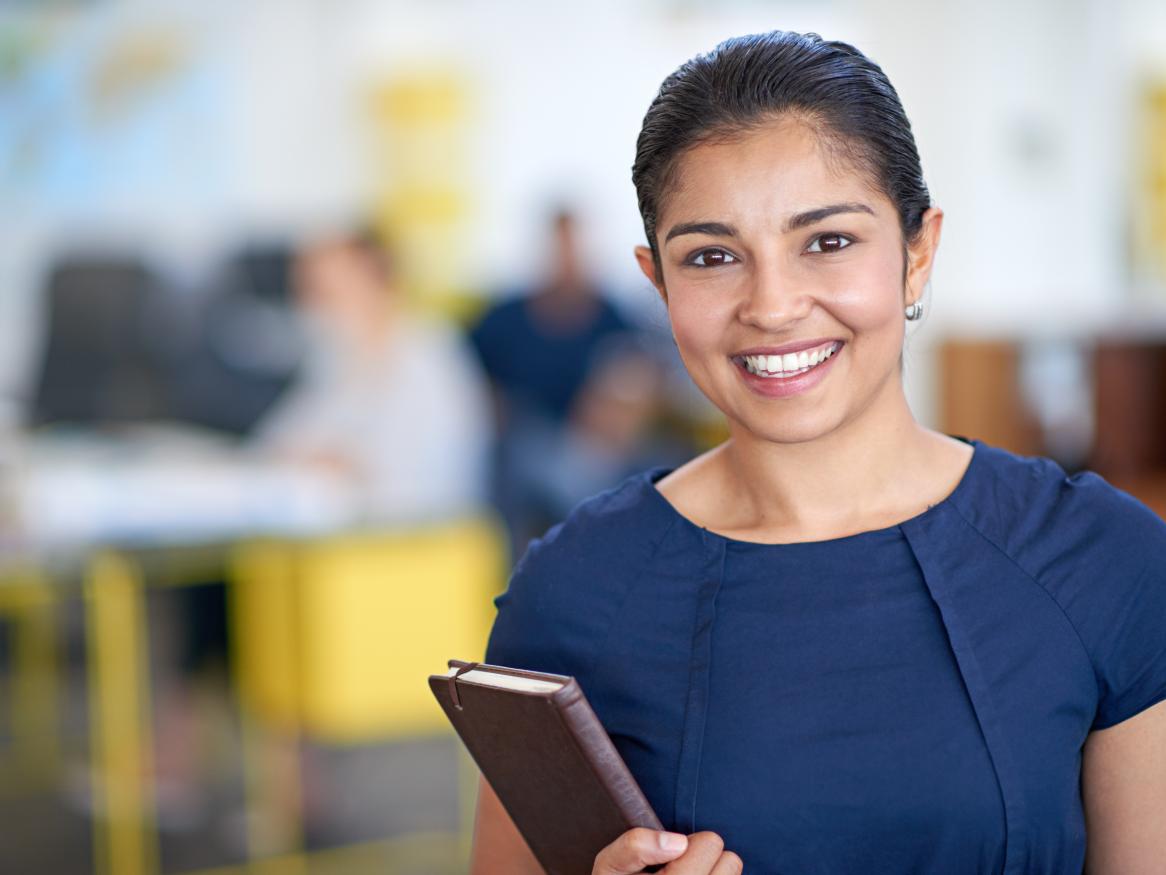 Female smiling, holding a notepad, in an office.